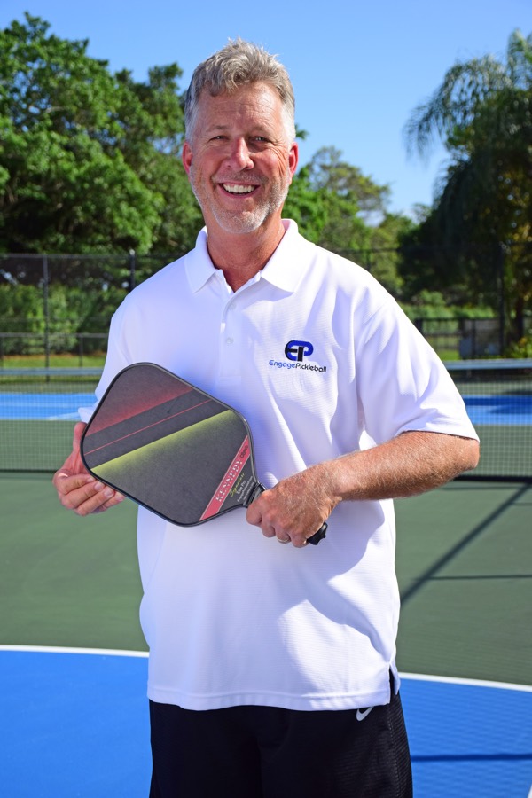 Steve Kennedy on court in a coaching polo, paddle in hand